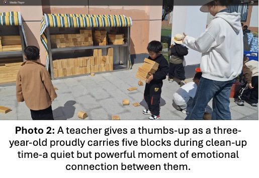 Photo 2. A teacher gives a thumbs-up as a three-year-old proudly carries five blocks during clean-up time — a quiet but powerful moment of emotional connection between them.